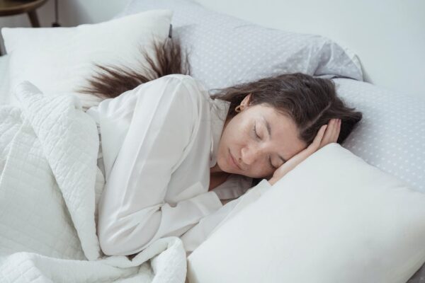 A serene woman rests comfortably in bed with soft pillows and blankets, embracing relaxation.