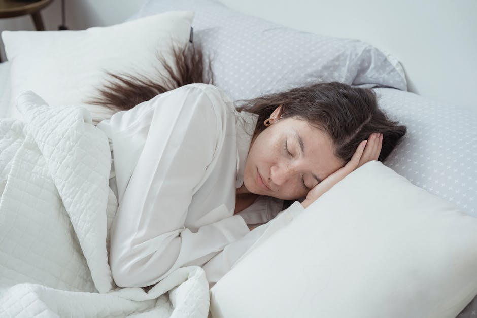 A serene woman rests comfortably in bed with soft pillows and blankets, embracing relaxation.