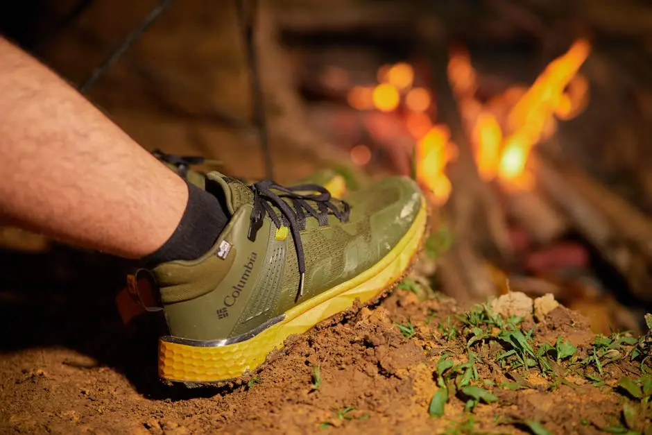 Primer plano de una bota de montaña verde cerca de una fogata, enfatizando la aventura al aire libre.