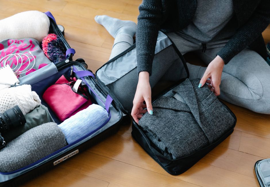 Woman organizes clothing and camera gear in a suitcase for travel.
