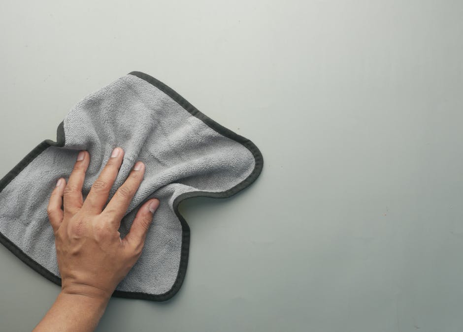 A hand wipes a light-colored table using a gray microfiber cloth, ideal for cleaning concepts.