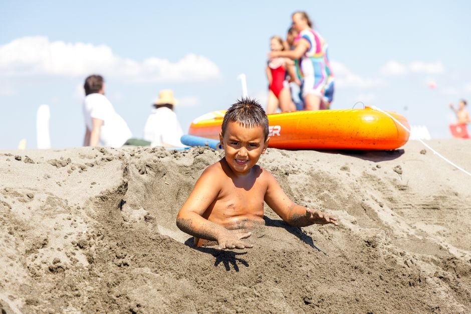 Niño jugando en la arena en un día soleado en la playa con aguas tranquilas