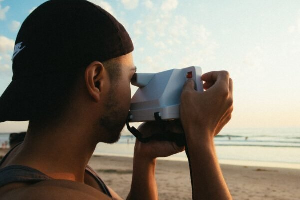 Persona haciendo una foto con cámara instantánea en la playa al atardecer durante un viaje