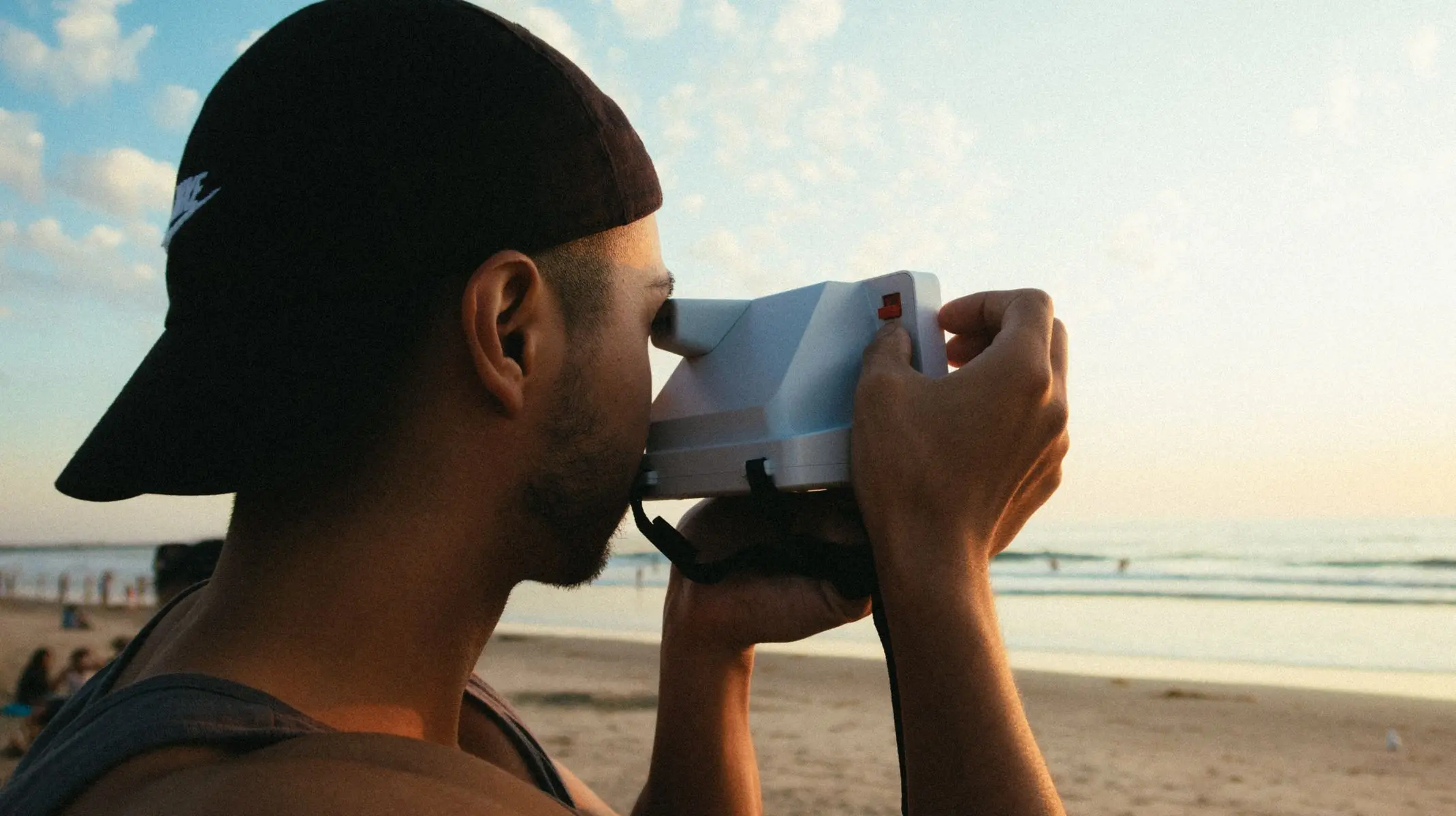 Persona haciendo una foto con cámara instantánea en la playa al atardecer durante un viaje