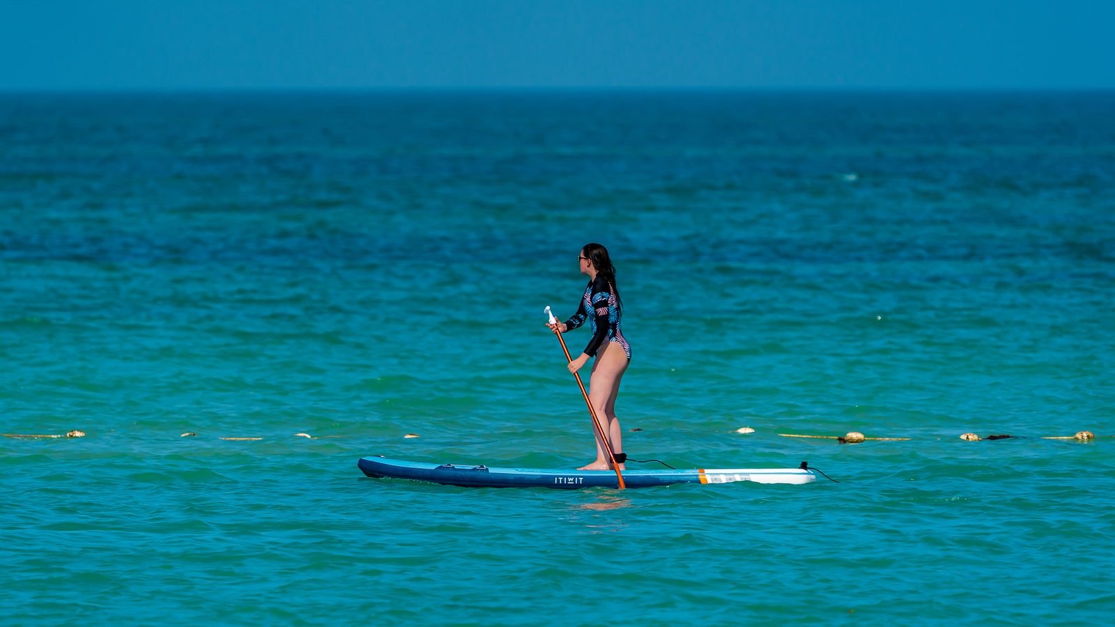 Mujer practicando paddle surf en un mar claro y tranquilo
