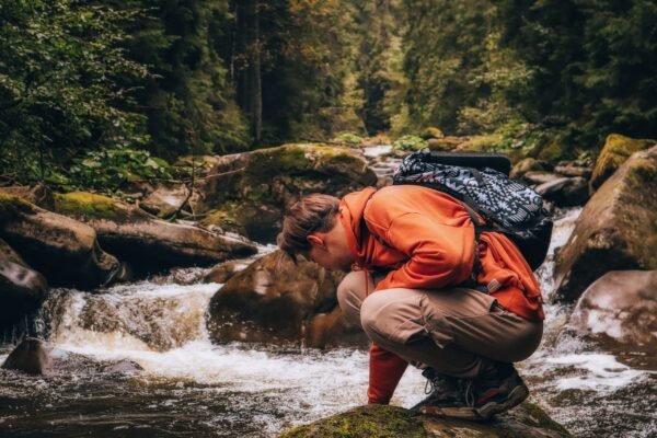 Excursionista filtrando agua de un arroyo de montaña durante una ruta de senderismo
