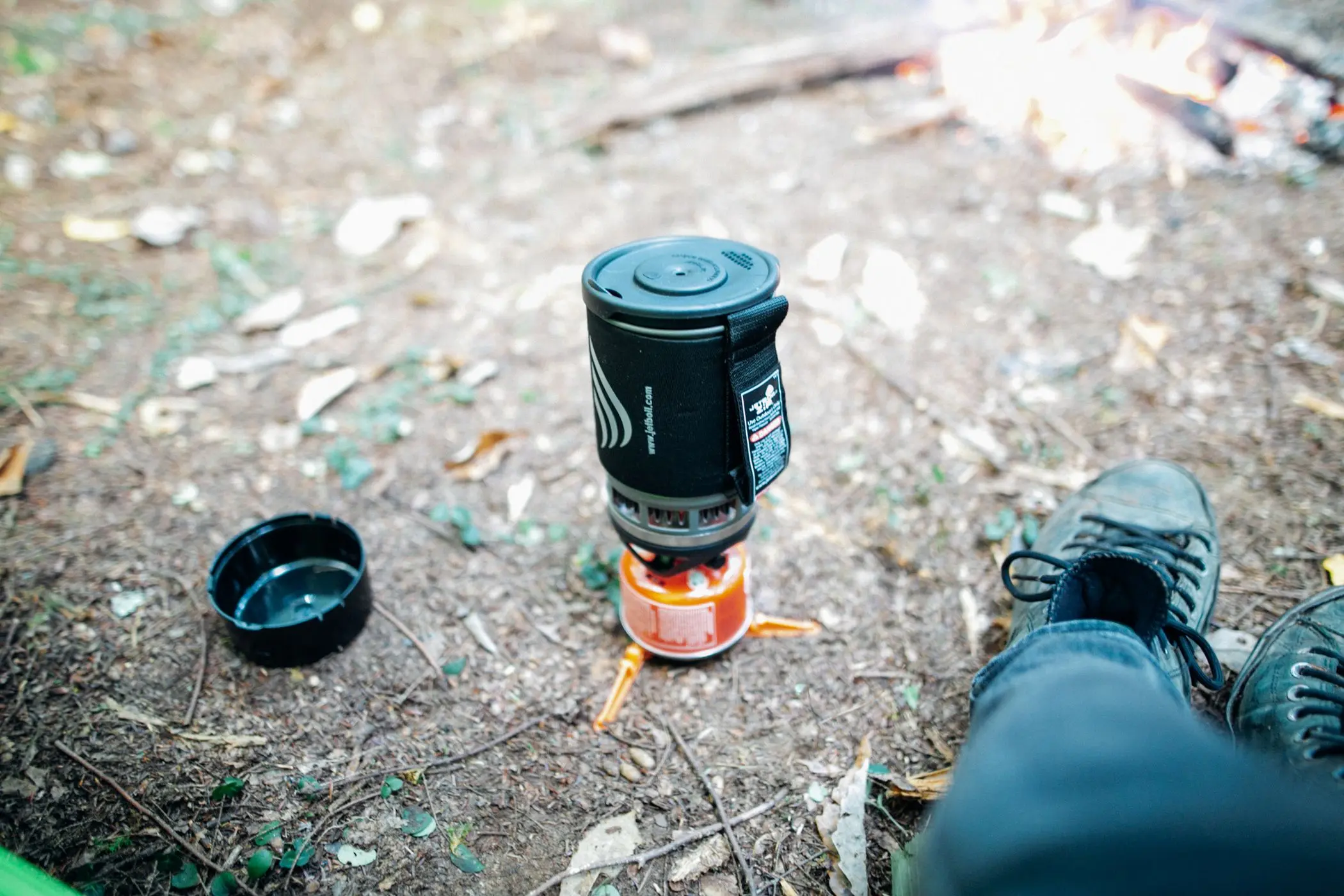 Viajero junto a una hoguera con un hornillo de camping compacto y ligero en un bosque de otoño