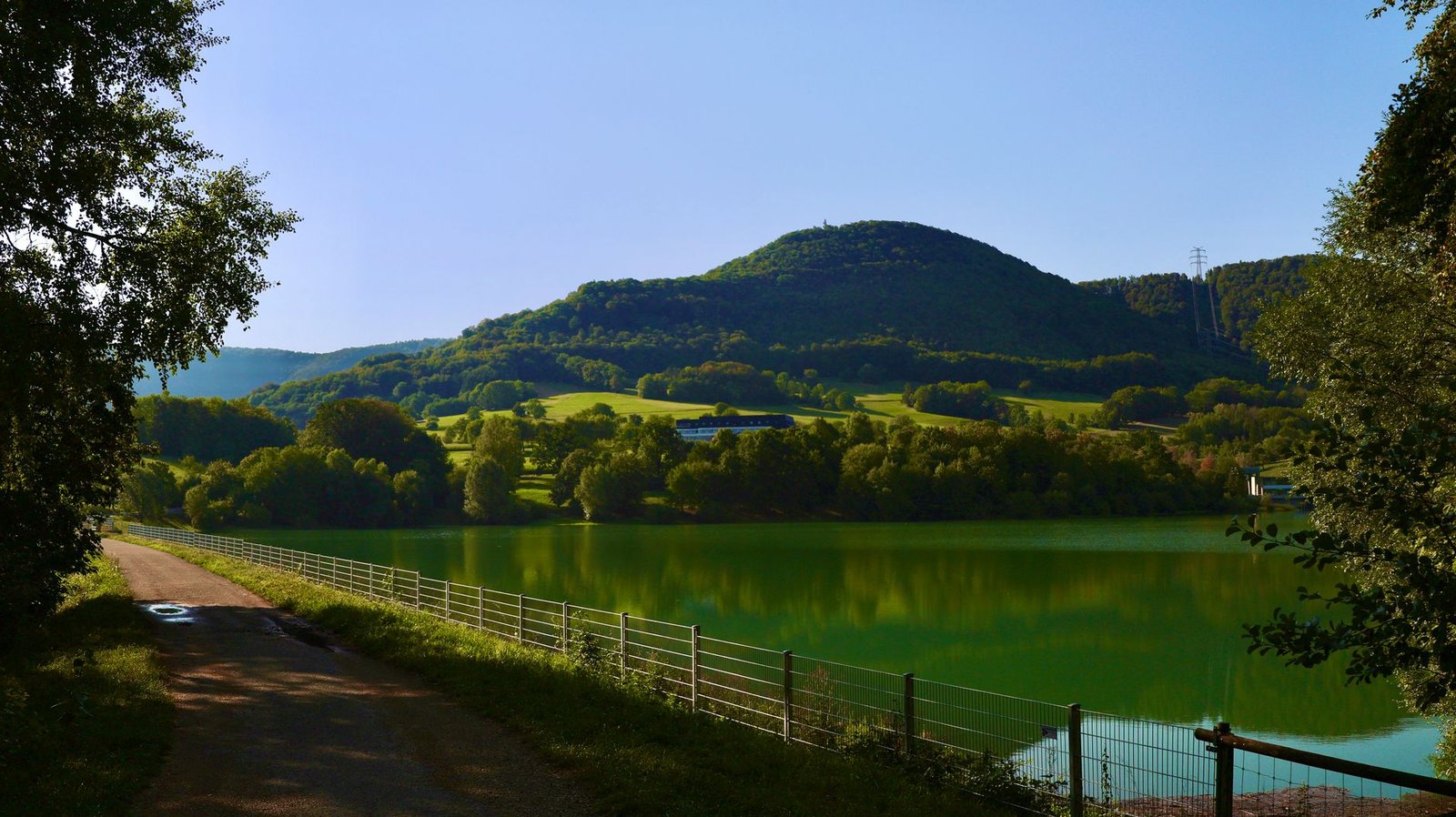 Lago tranquilo rodeado de colinas verdes bajo un cielo azul, el refugio perfecto para huir de las multitudes