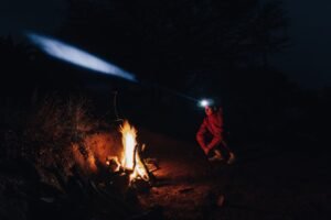 Hombre con linterna frontal iluminando la noche junto a una fogata de camping