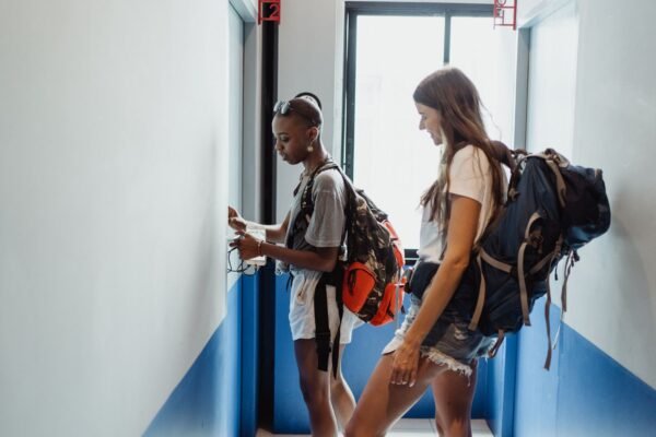 Dos mujeres viajeras en un corredor de albergue con mochilas, preparándose para su viaje.