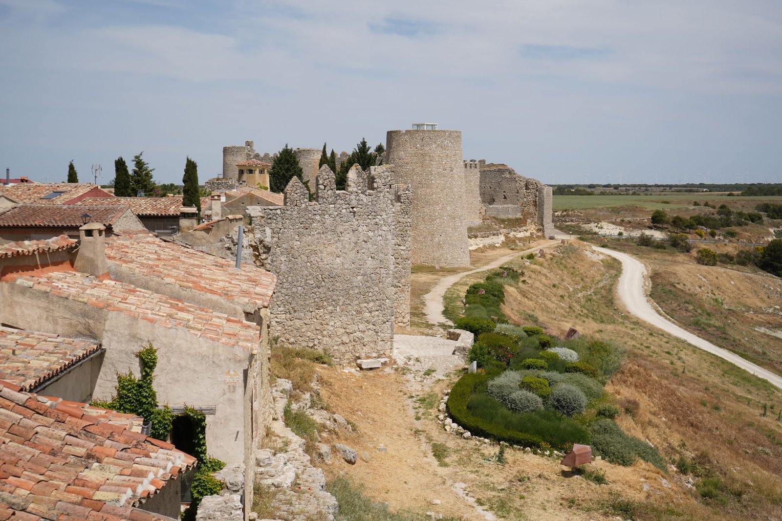 Murallas y torreones de piedra de un castillo medieval sobre un paisaje campestre.