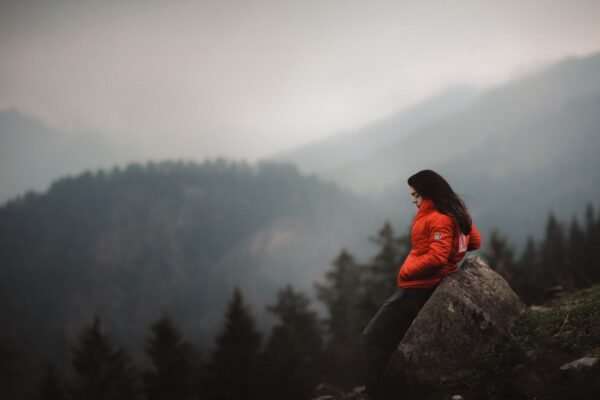 Viajera con chaqueta acolchada roja apoyada en una roca frente a un paisaje de montaña