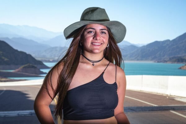 Viajera con sombrero de ala ancha ante un lago de montaña en un día soleado