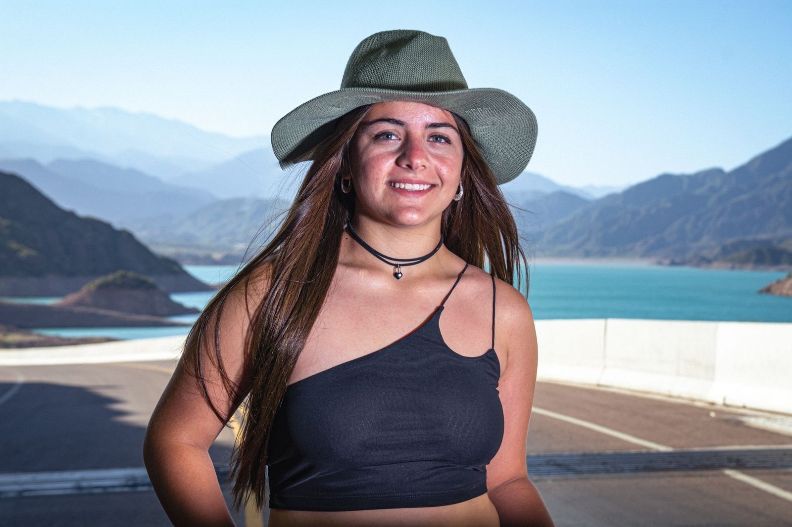 Viajera con sombrero de ala ancha ante un lago de montaña en un día soleado