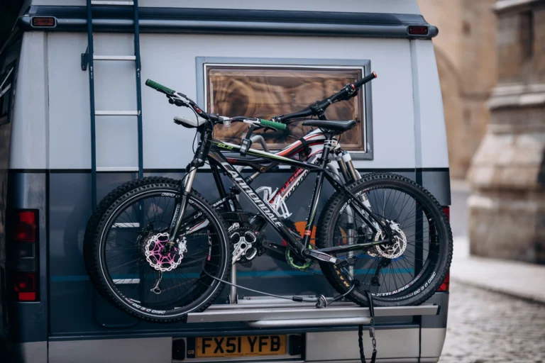 Dos bicicletas de montaƱa sujetas en un portabicicletas trasero sobre una camper aparcada en la montaƱa
