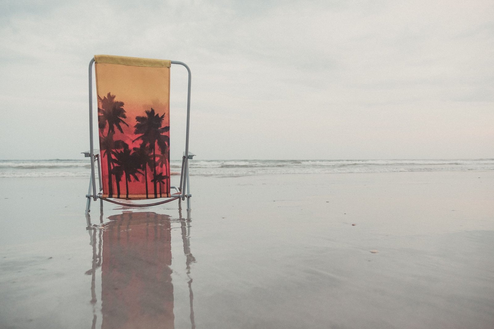 Silla de playa plegable con diseño de palmera en la arena junto al mar