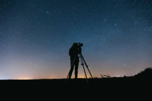 Persona observando el cielo estrellado con un telescopio portátil de noche