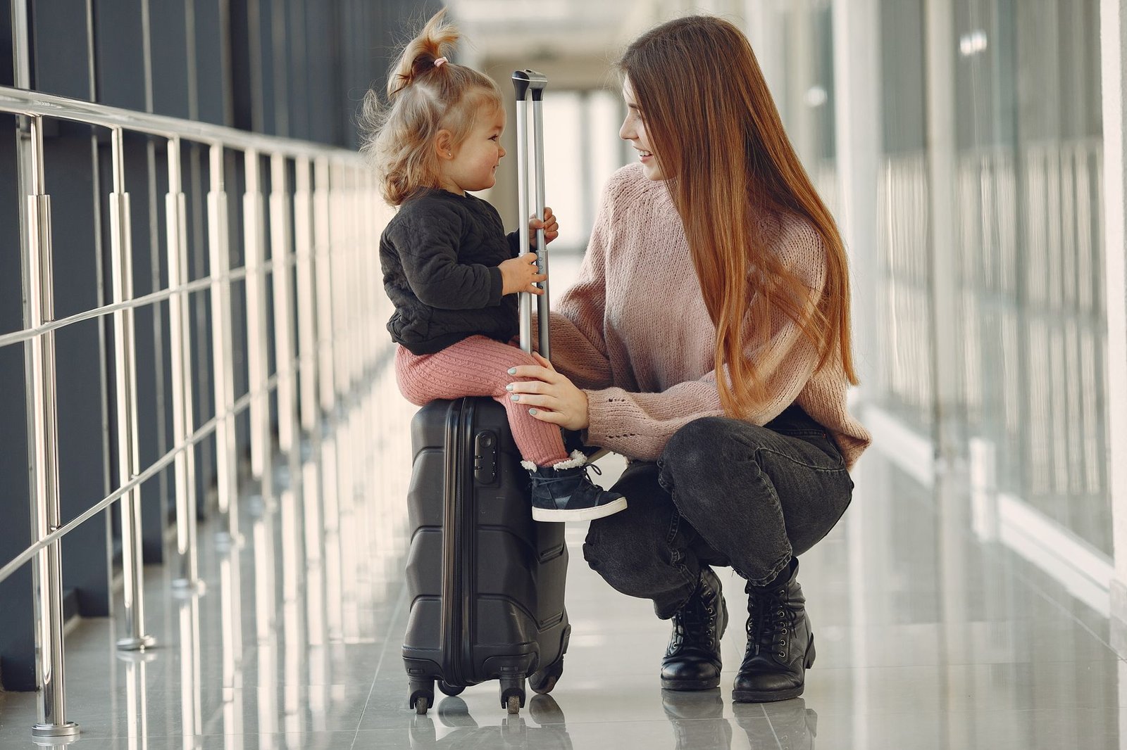 Madre e hija sentadas sobre una maleta esperando en el aeropuerto