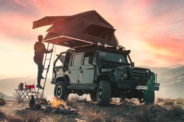Viajero subiendo a una tienda de techo instalada sobre un todoterreno al atardecer en la montaña