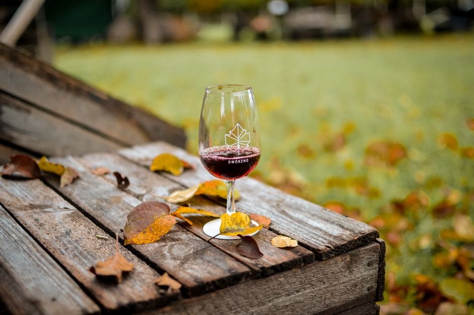 Copa de vino tinto en mesa rústica rodeada de hojas otoñales