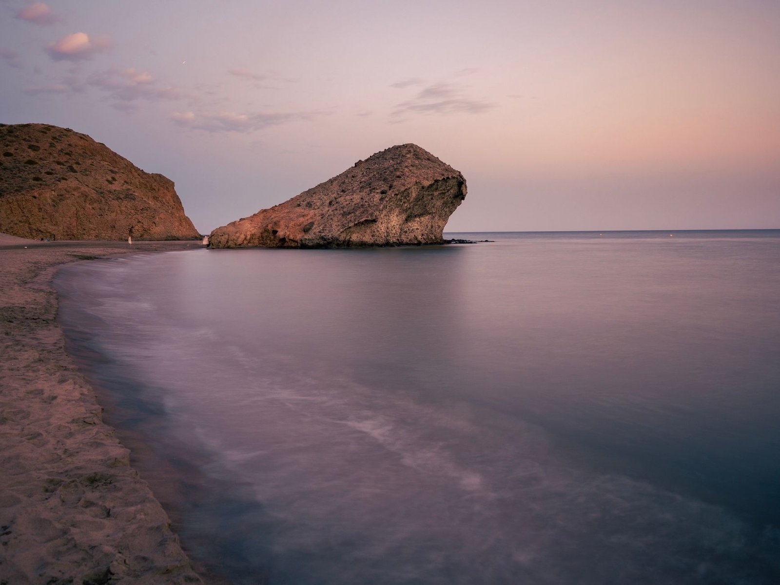 Formación rocosa en la costa de Almería al atardecer, con el mar en calma y el cielo pastel