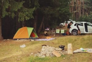 Tienda de campaña familiar montada junto al coche en un camping forestal