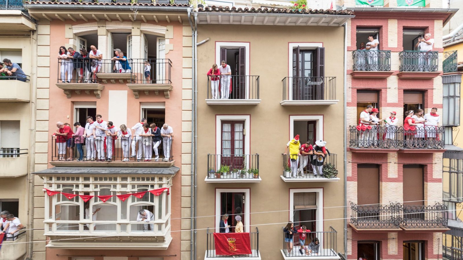 Multitud vestida de blanco y rojo observando desde los balcones durante las fiestas de San Fermín en Pamplona