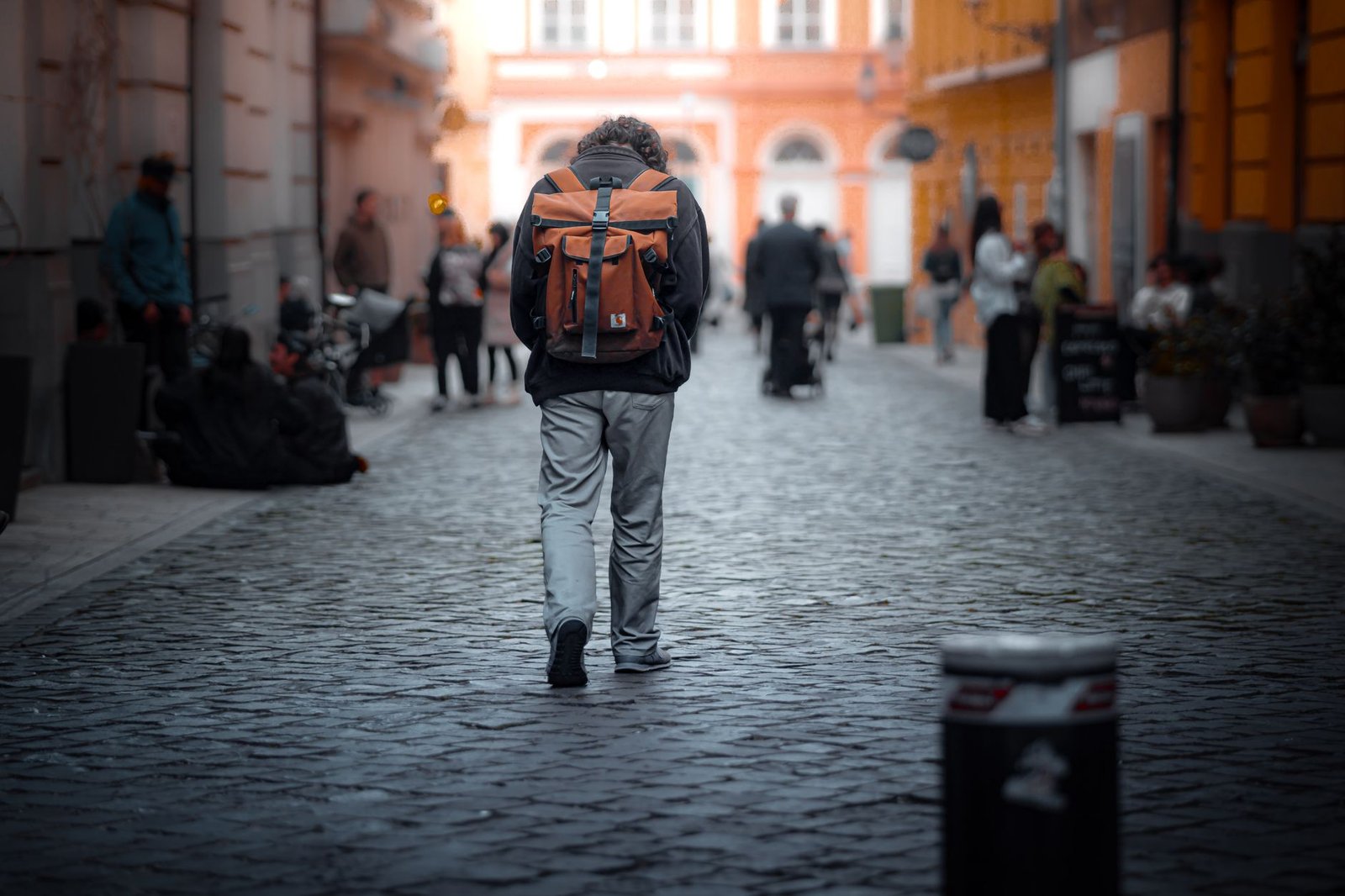 Viajero con mochila caminando solo por una calle adoquinada entre gente en la ciudad
