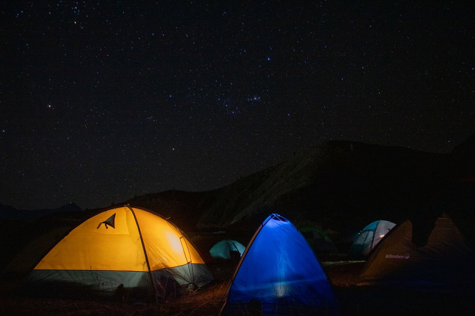 Tiendas de campaña iluminadas bajo un cielo estrellado en un campamento de montaña