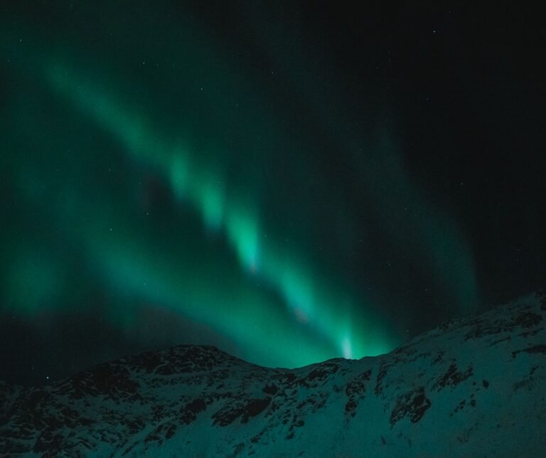 Aurora boreal verde sobre montañas nevadas en un cielo nocturno estrellado