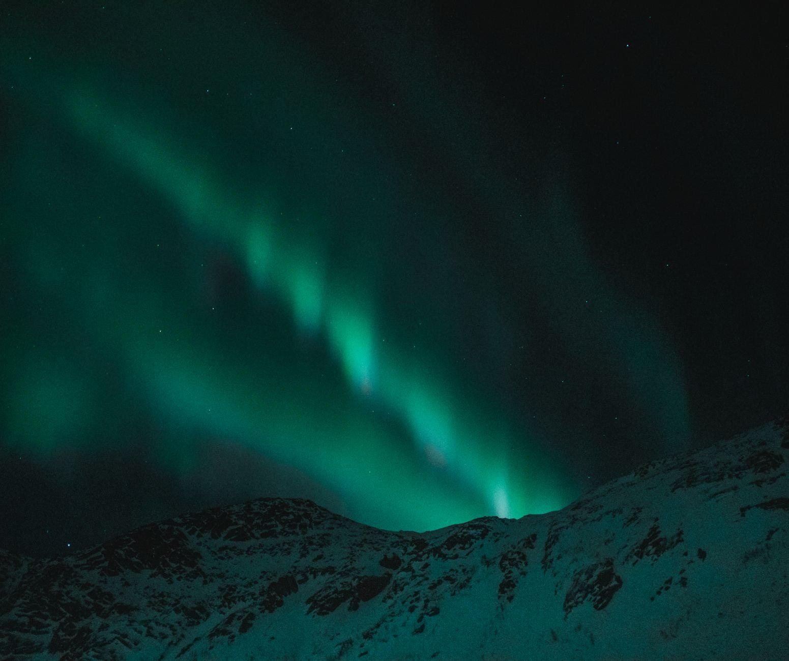 Aurora boreal verde sobre montañas nevadas en un cielo nocturno estrellado