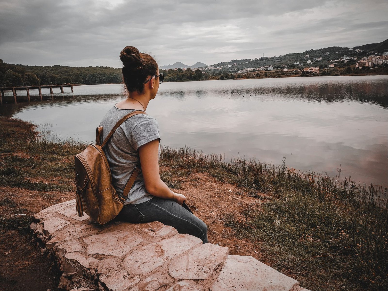 Mujer sentada en un muro de piedra junto a un lago en Albania