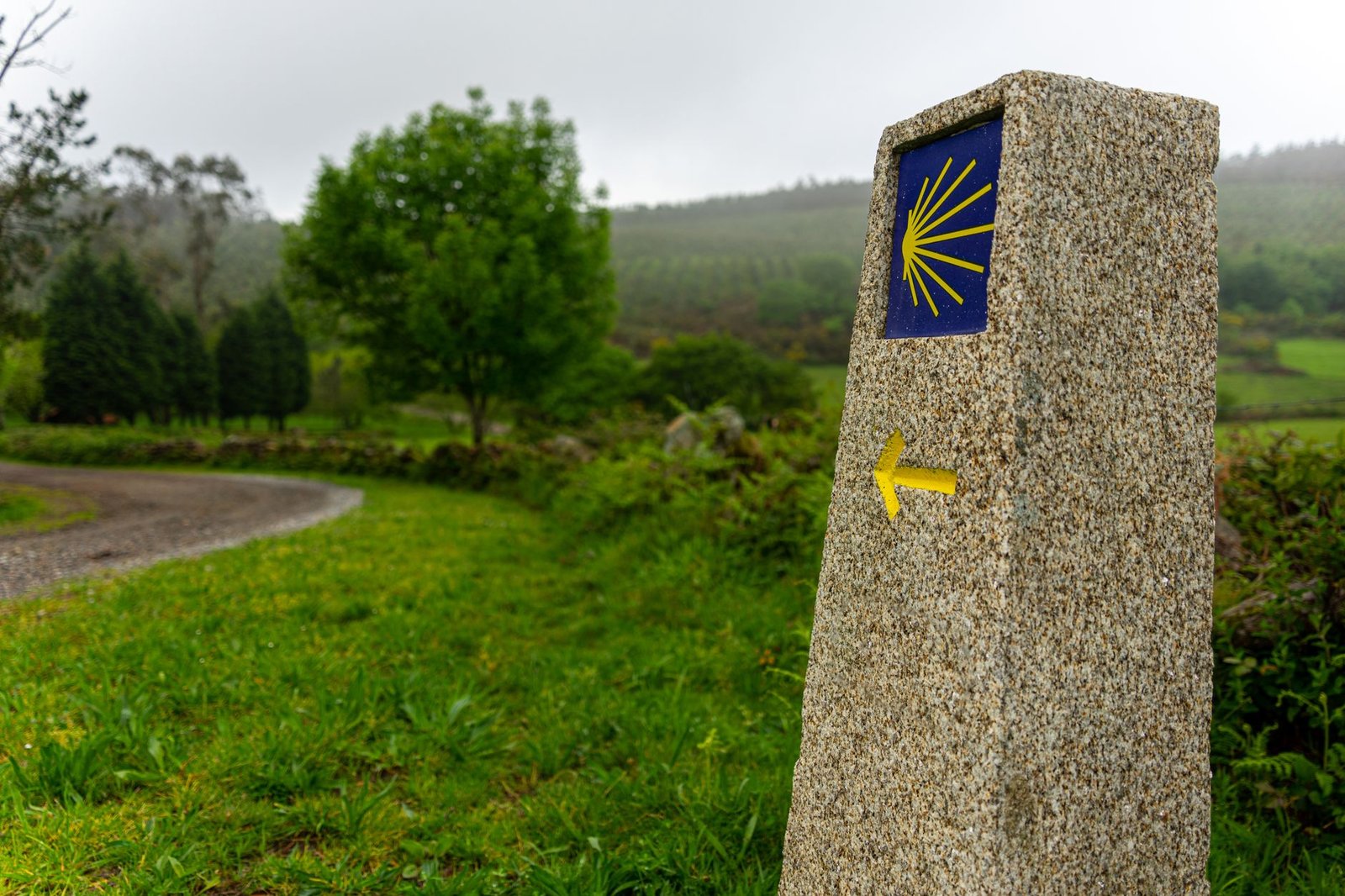 Mojón de señalización del Camino de Santiago con la concha y la flecha amarilla