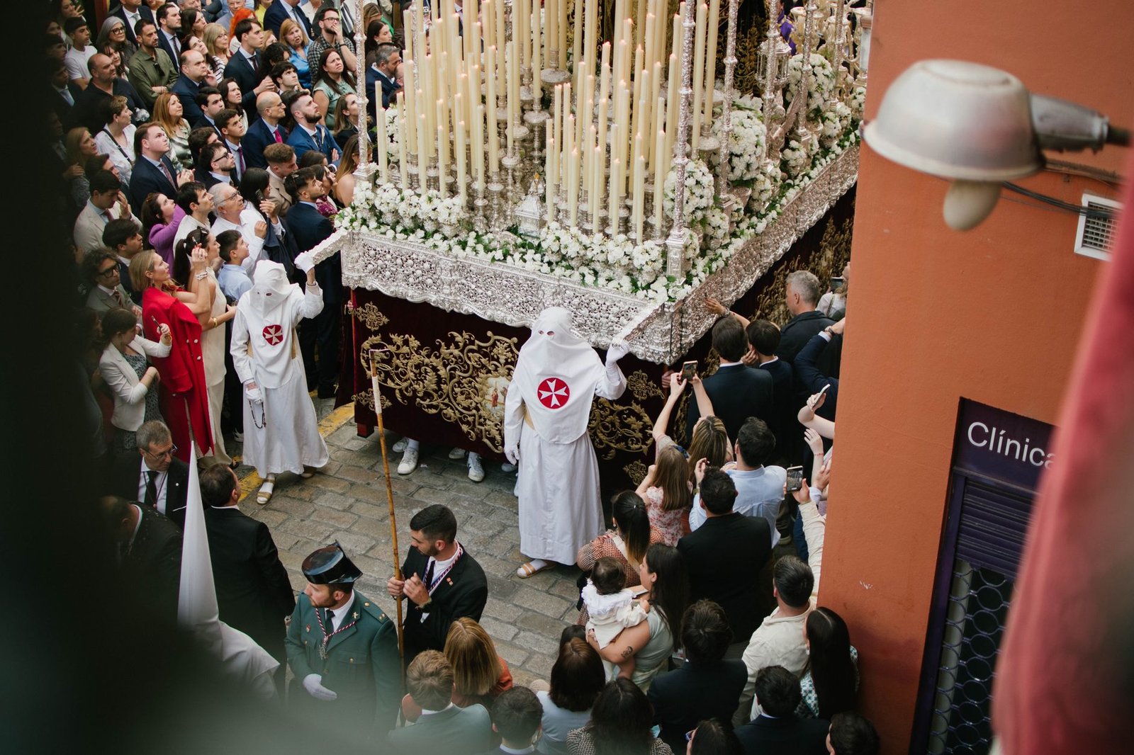 Cofradía de Semana Santa con túnicas y cirios avanzando por una calle de Sevilla