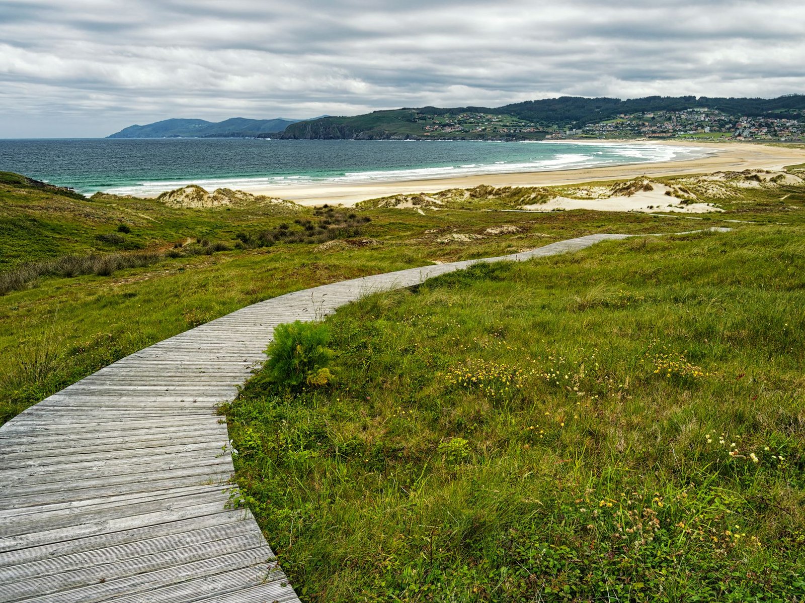 Pasarela de madera sobre las dunas hacia una playa de arena blanca en Galicia