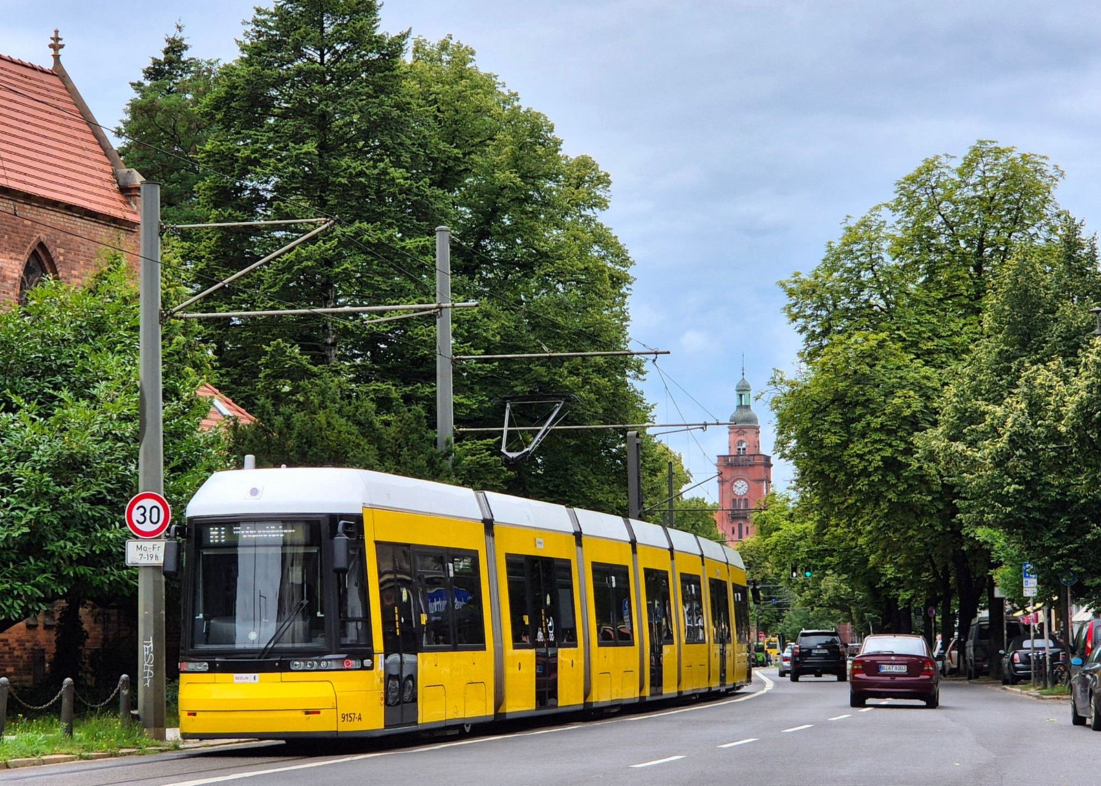 Tranvía amarillo por una calle arbolada de Berlín con una iglesia histórica al fondo