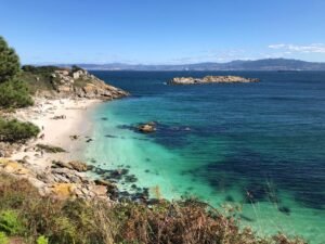Cala de arena y roca con agua turquesa y cielo azul en la costa atlántica gallega