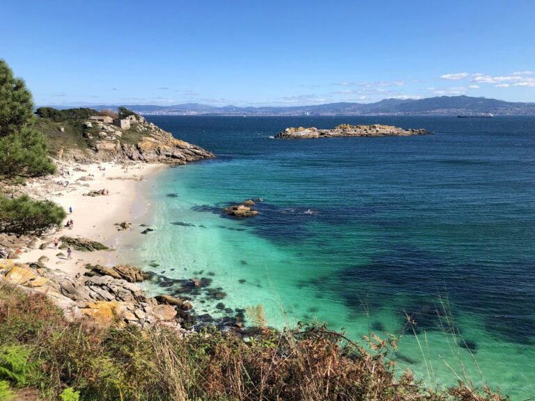 Cala de arena y roca con agua turquesa y cielo azul en la costa atlántica gallega