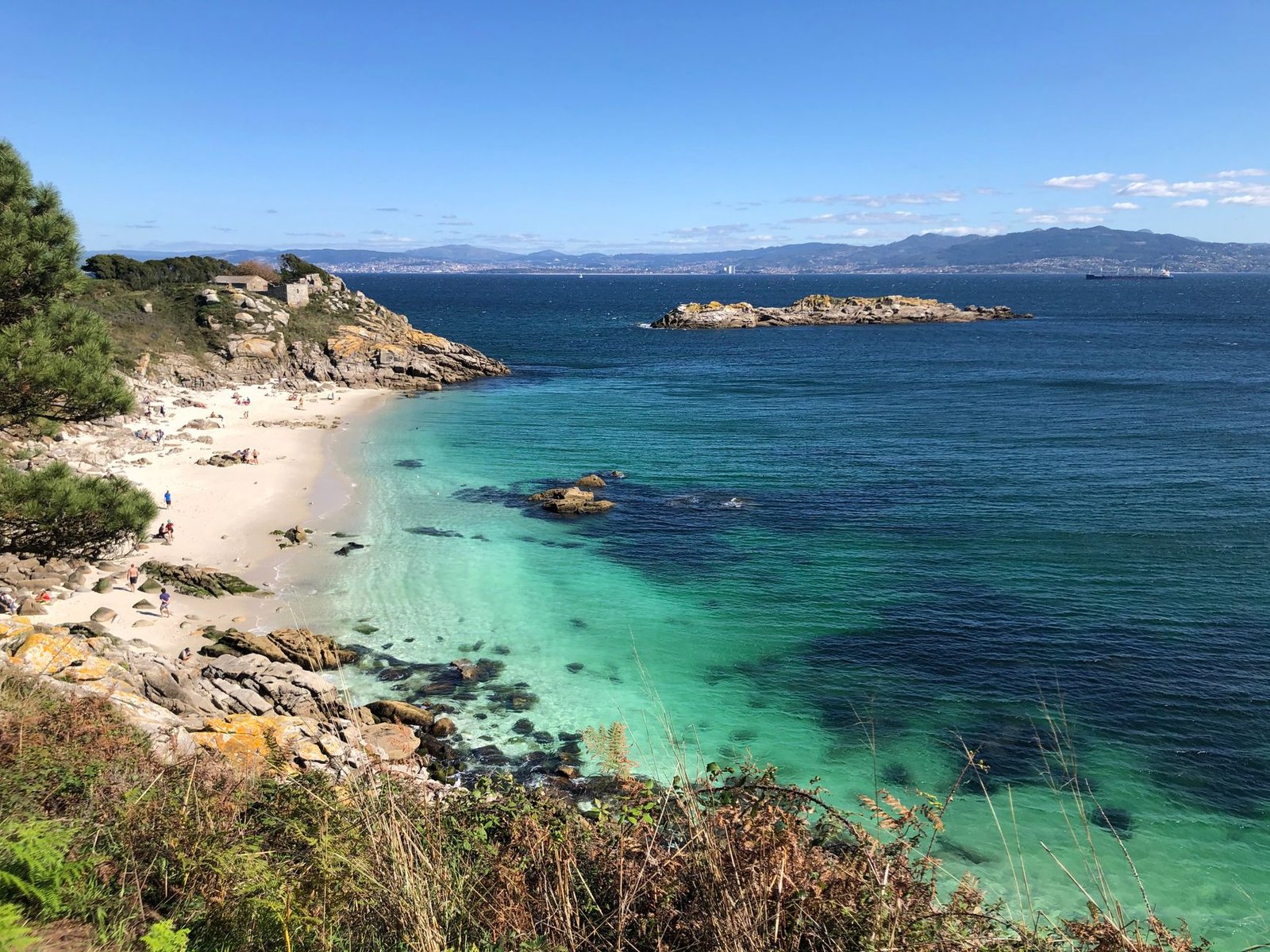 Cala de arena y roca con agua turquesa y cielo azul en la costa atlántica gallega