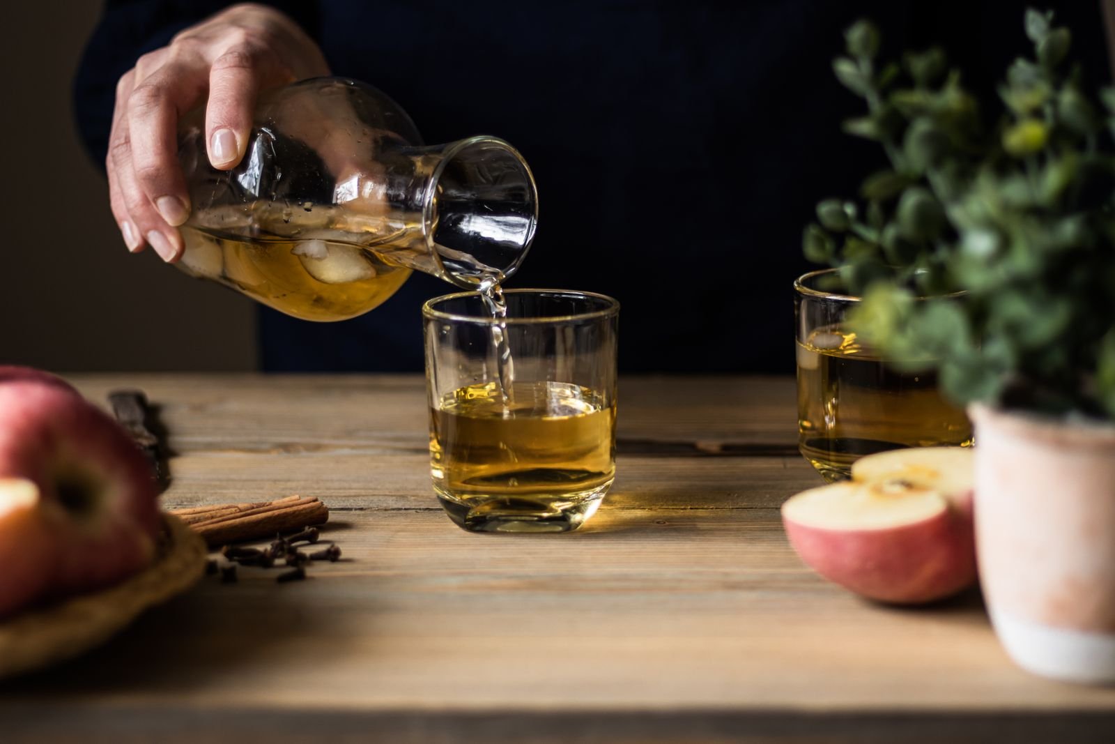 Sidra siendo vertida en un vaso de vidrio junto a manzanas frescas