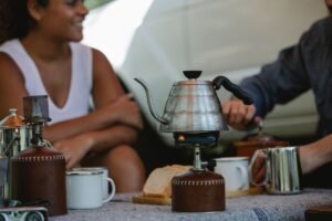 Pareja preparando café con hervidor sobre un hornillo de gas portátil durante una acampada