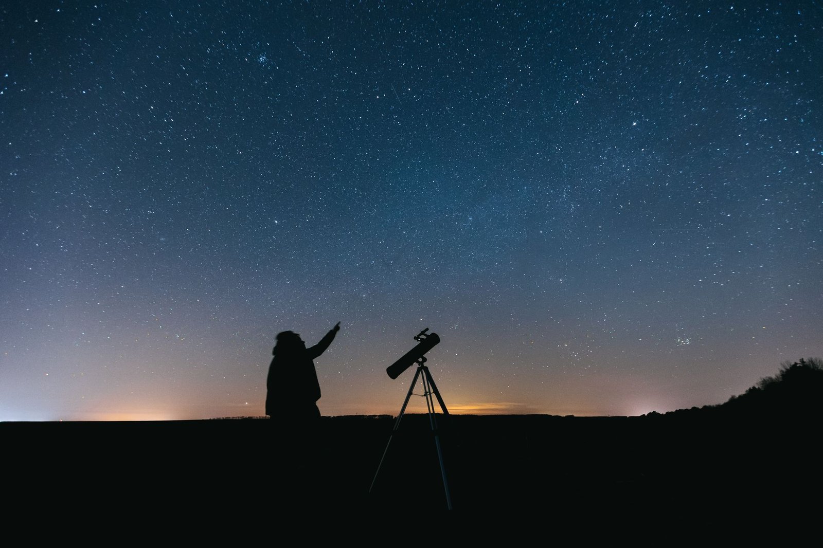 Silueta de una persona observando el cielo estrellado con un telescopio por la noche