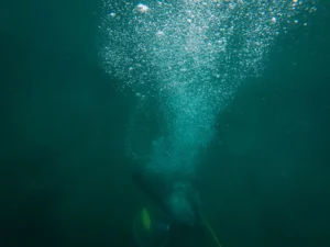 Buceador con botella de aire comprimido dejando un rastro de burbujas bajo el agua