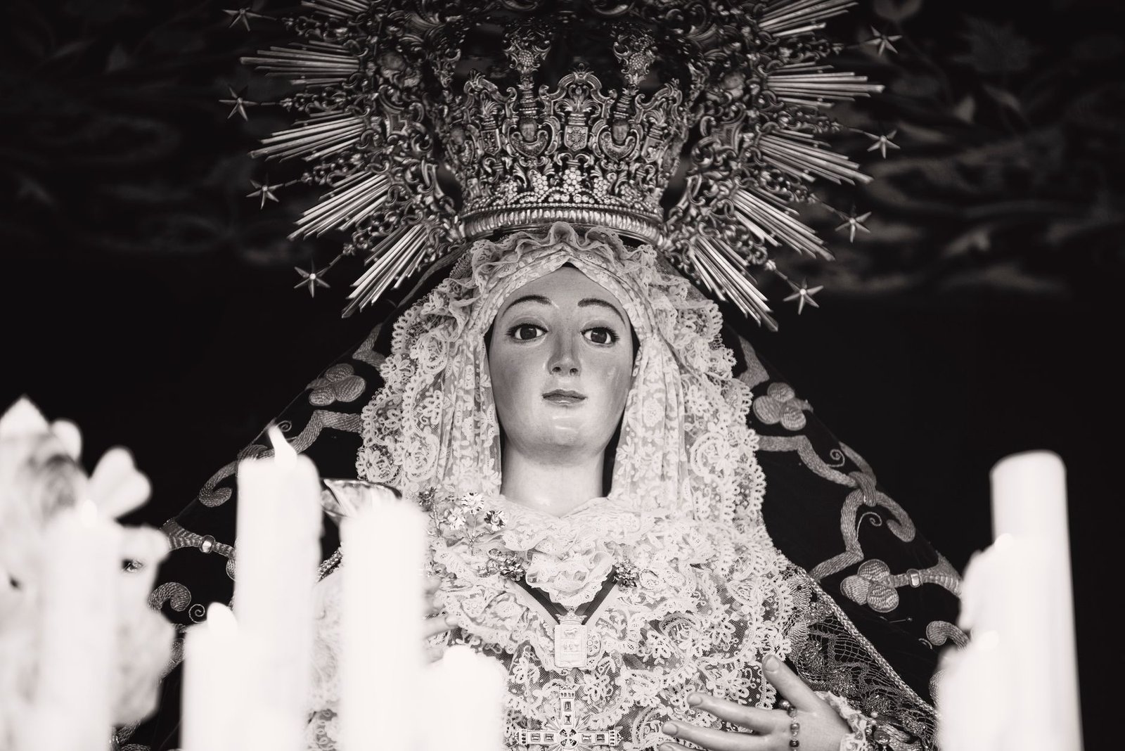 Cirios encendidos ante una imagen religiosa en la penumbra durante la Semana Santa de Sevilla
