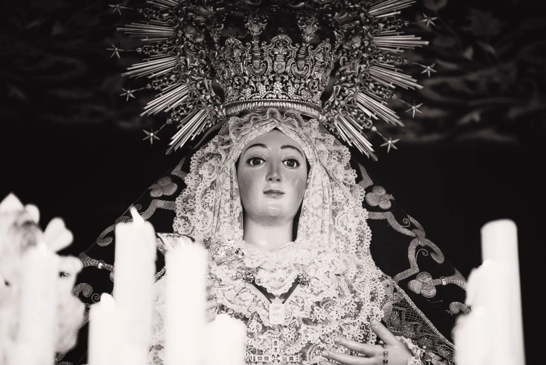 Cirios encendidos ante una imagen religiosa en la penumbra durante la Semana Santa de Sevilla