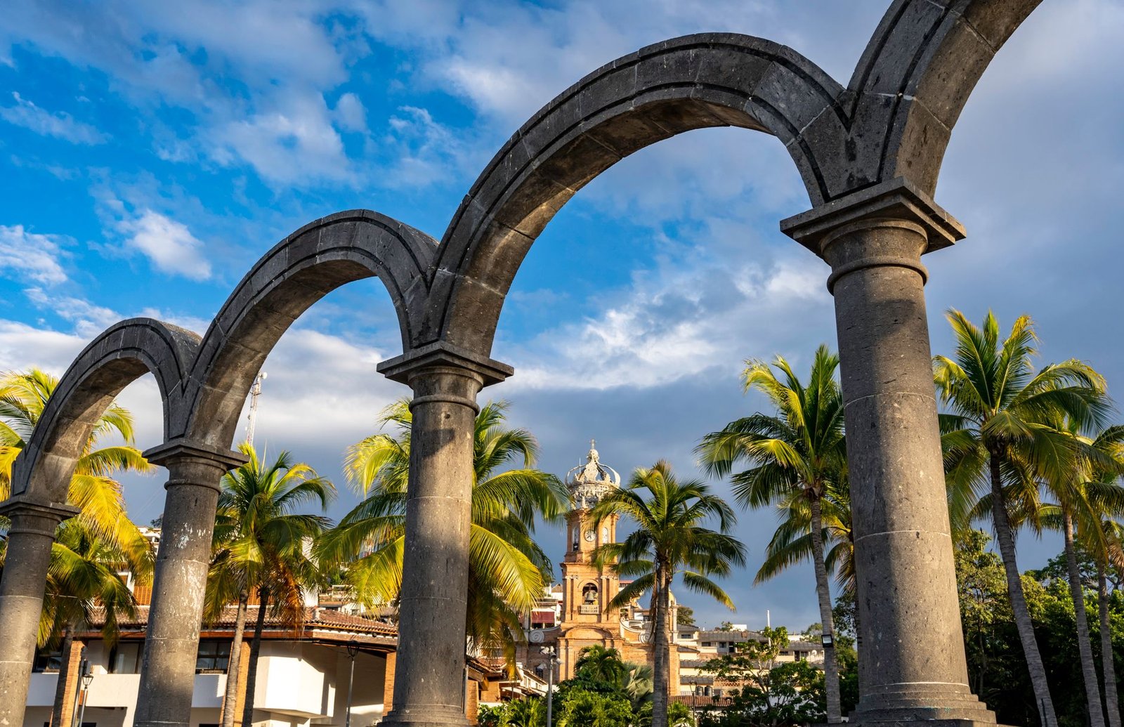 Arcos de piedra del Malecón de Puerto Vallarta con la torre coronada de la parroquia al fondo