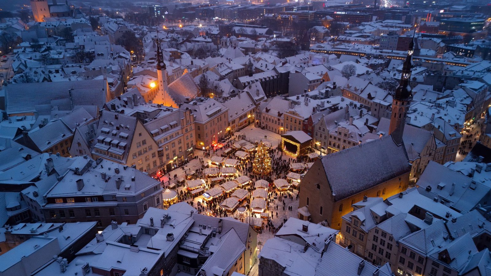 Mercado de Navidad nevado en la plaza del Ayuntamiento de Tallin, con el casco antiguo iluminado