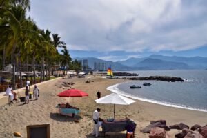 Playa de Puerto Vallarta con palmeras, sombrillas y un velero con las montañas al fondo