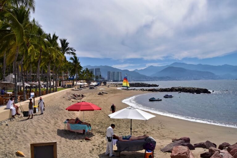 Playa de Puerto Vallarta con palmeras, sombrillas y un velero con las montañas al fondo