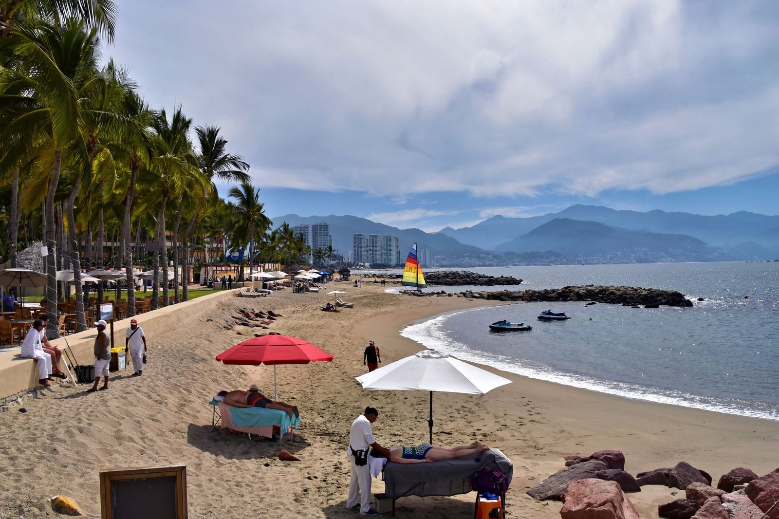 Playa de Puerto Vallarta con palmeras, sombrillas y un velero con las montañas al fondo